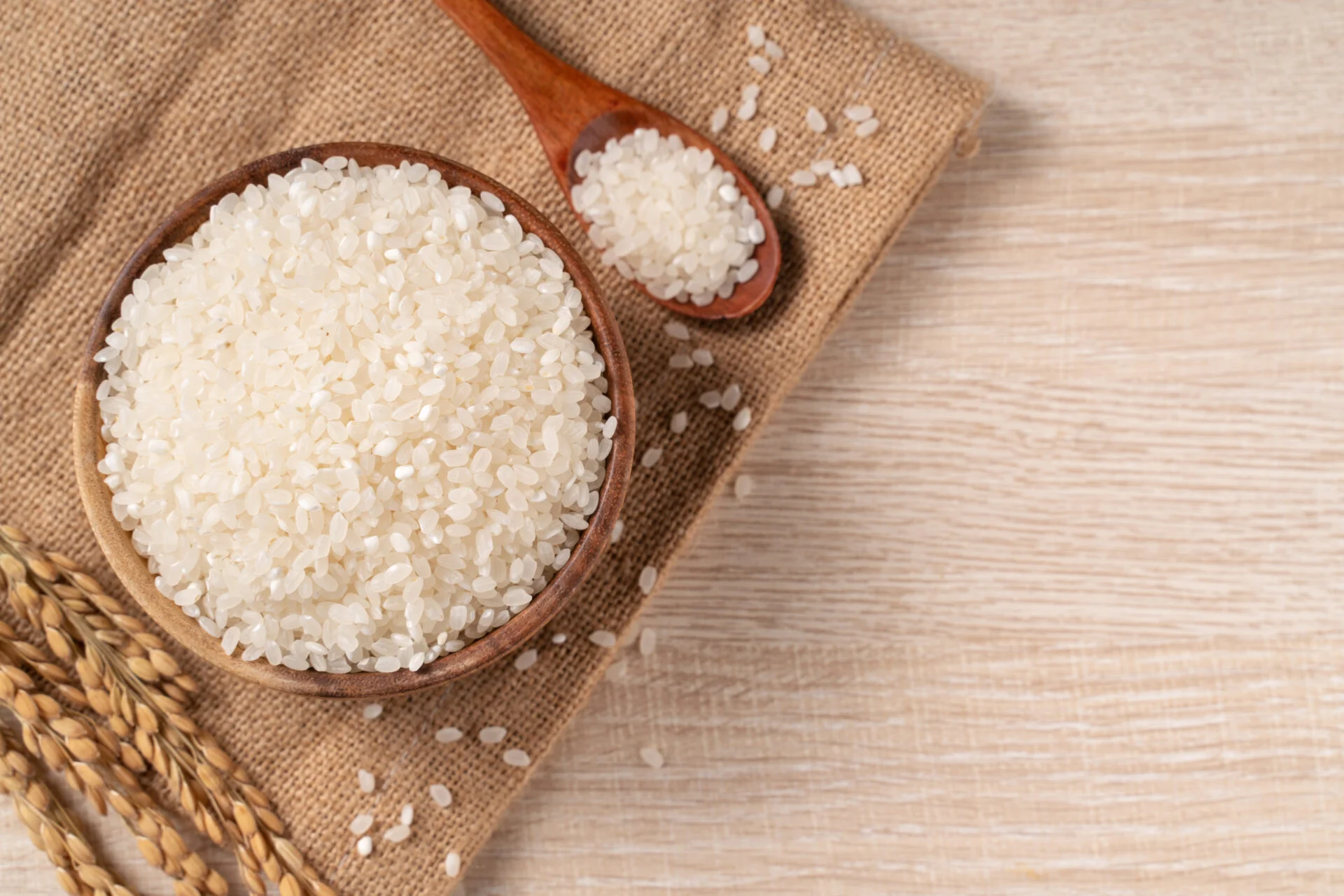 White raw rice in a bowl with the ear on the wooden table background