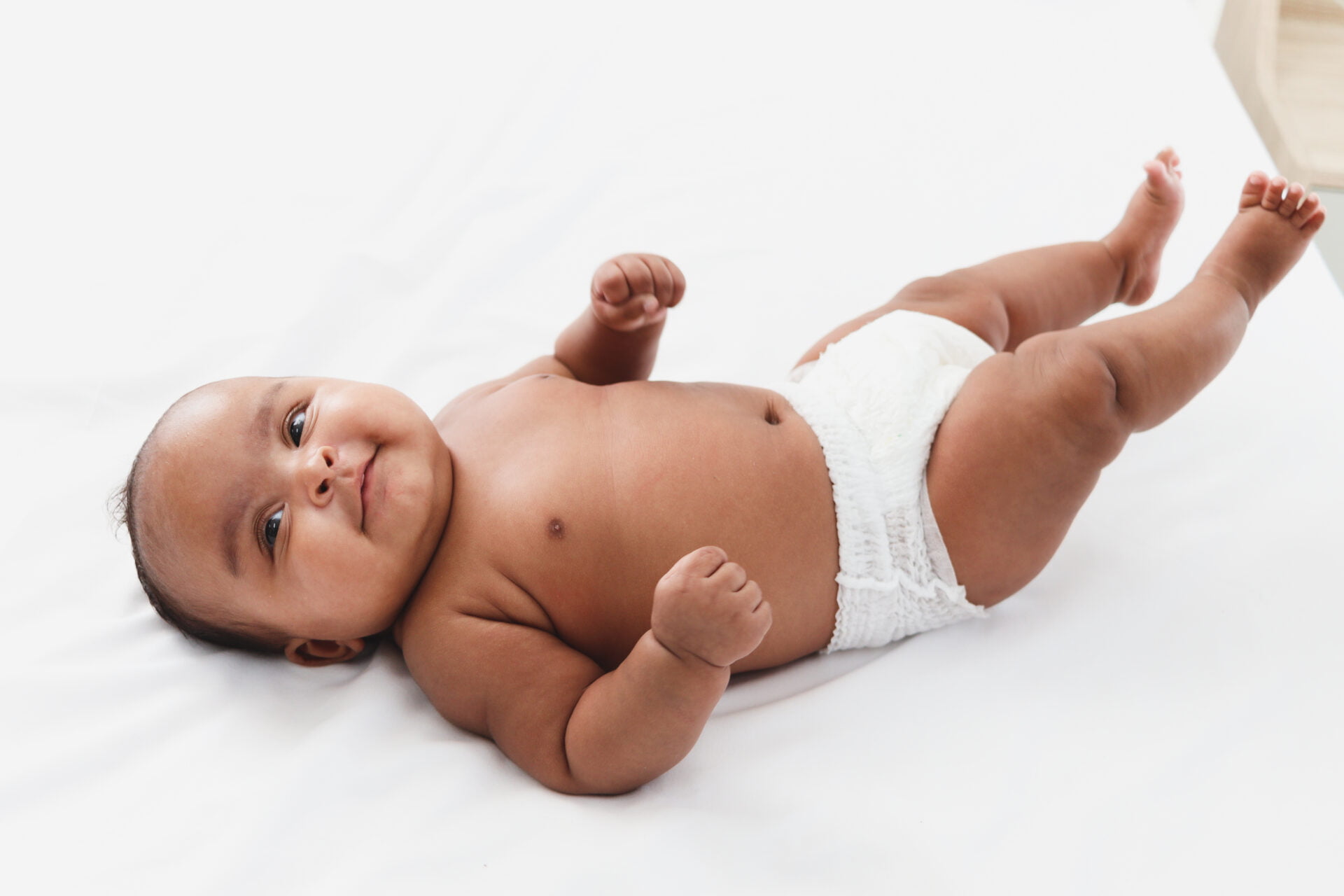 Happy little newborn baby girl lying on the white bed in the bedroom, portrait of sweet adorable infant baby.
