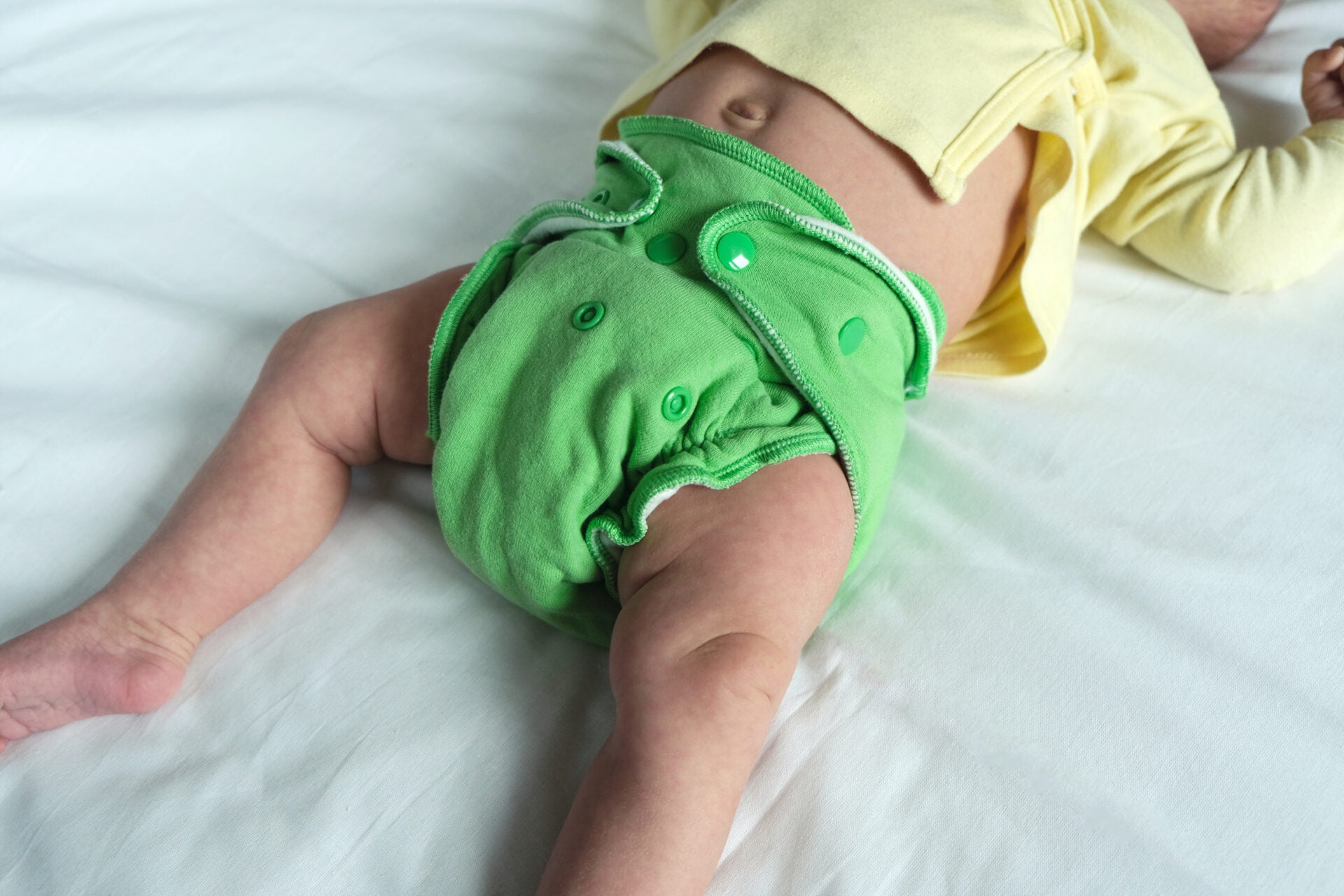 Newborn baby in green reusable diaper on a white sheet. Modern eco friendly cloth nappy for infant child hygiene. Sustainable lifestyle, zero waste concept.