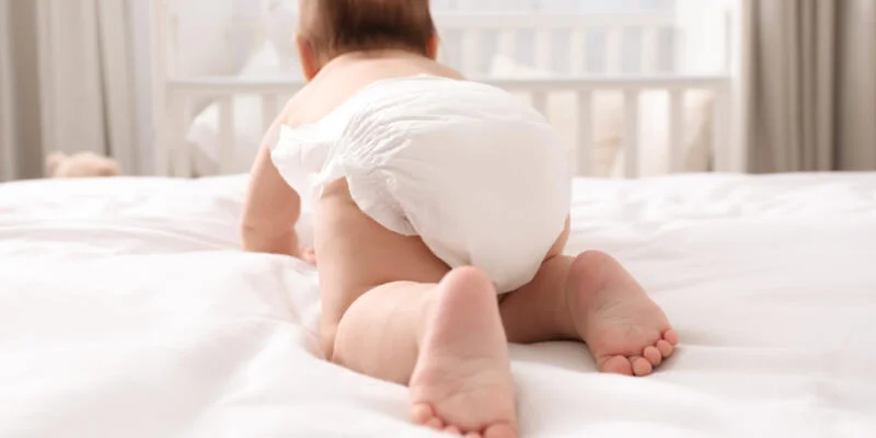 Little baby in diaper on bed at home, back view