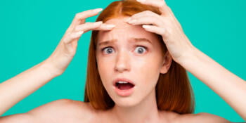 Anti acne. Close-up portrait of worried nice attractive red-haired girl with shiny pure clean skin, touching forehead, isolated over green turquoise background