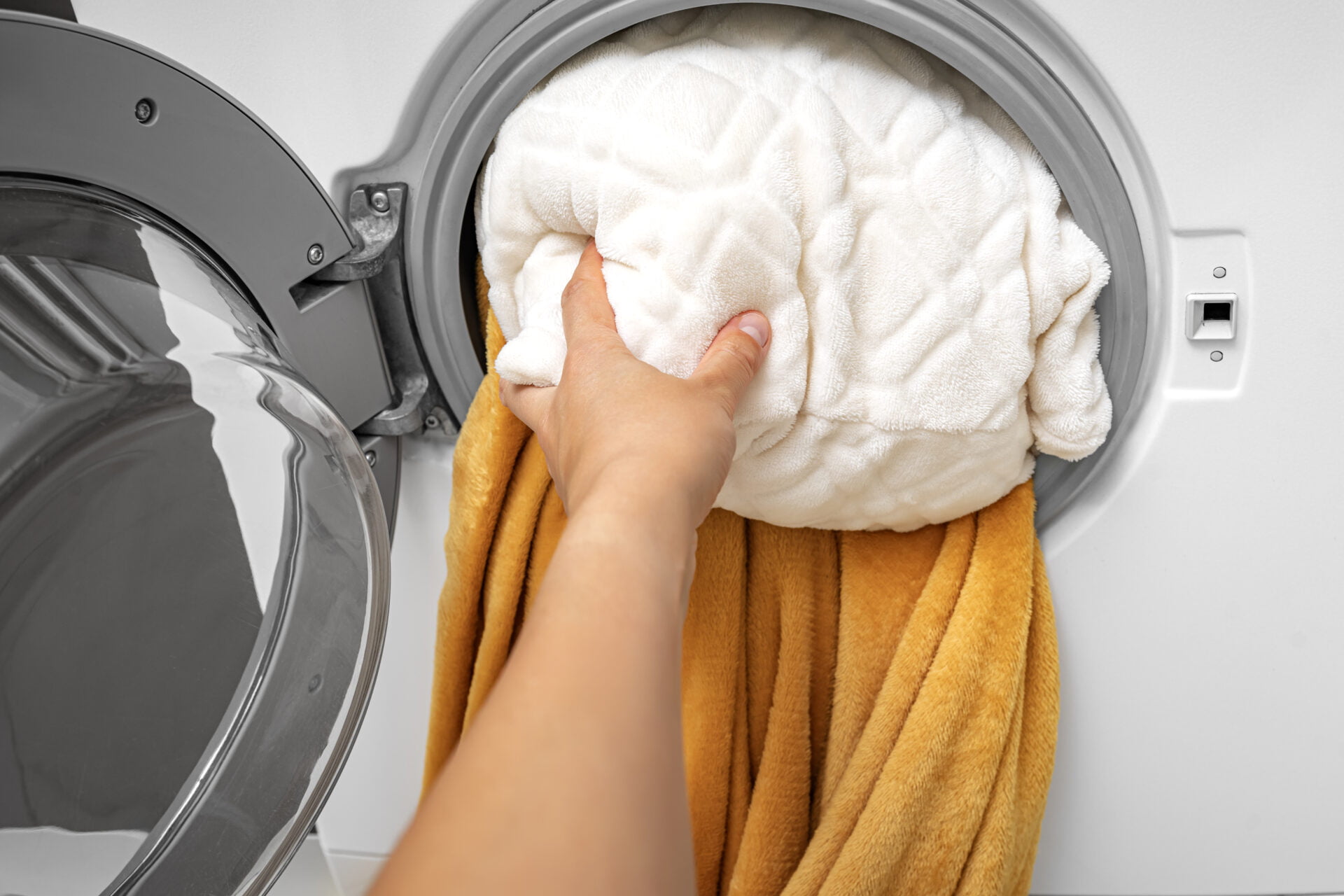 A hand pushes a pillow into the washing machine. Washing large items.