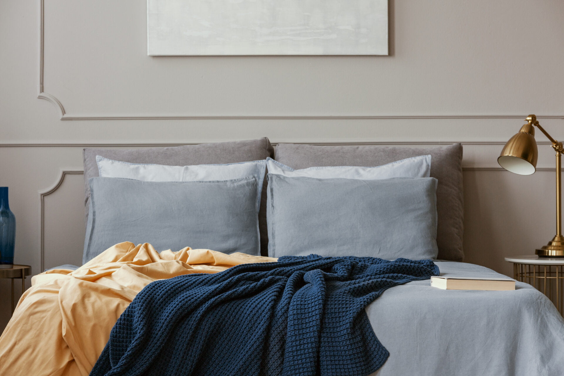 Dark blue and orange blankets on comfortable double bed in grey stylish bedroom