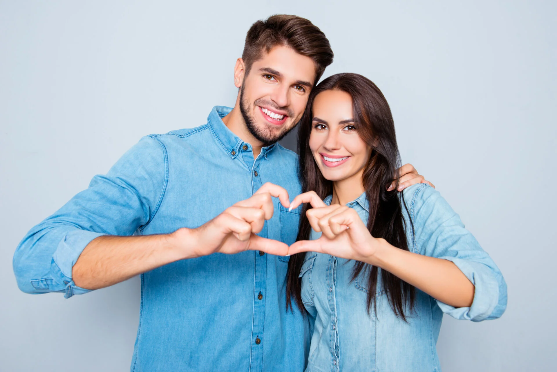 Cheerful smiling man and woman in love making heart with fingers