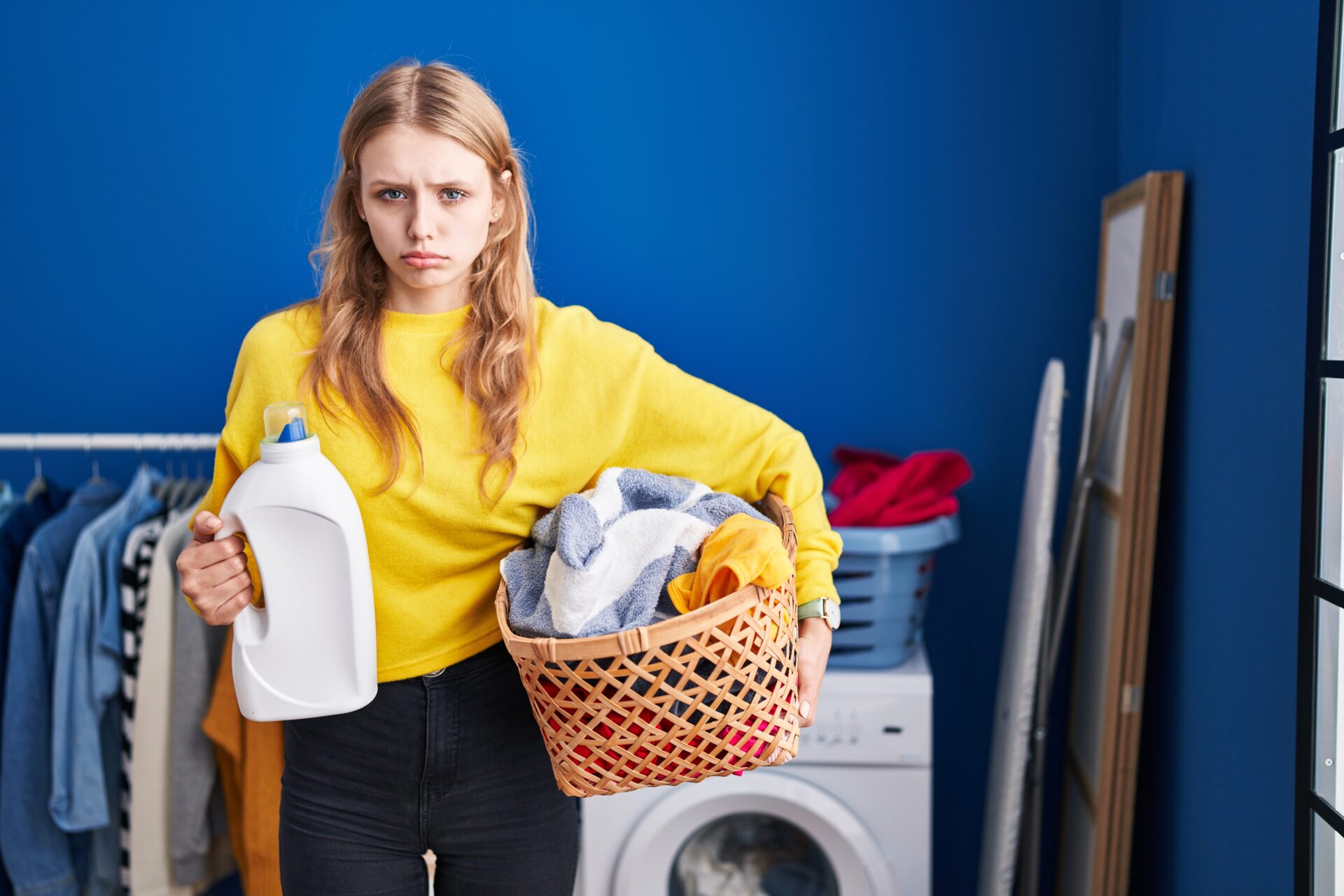 Young caucasian woman holding laundry basket and detergent bottle depressed and worry for distress, crying angry and afraid because her laundry detergent sheets may contain PFAS "forever chemicals". 