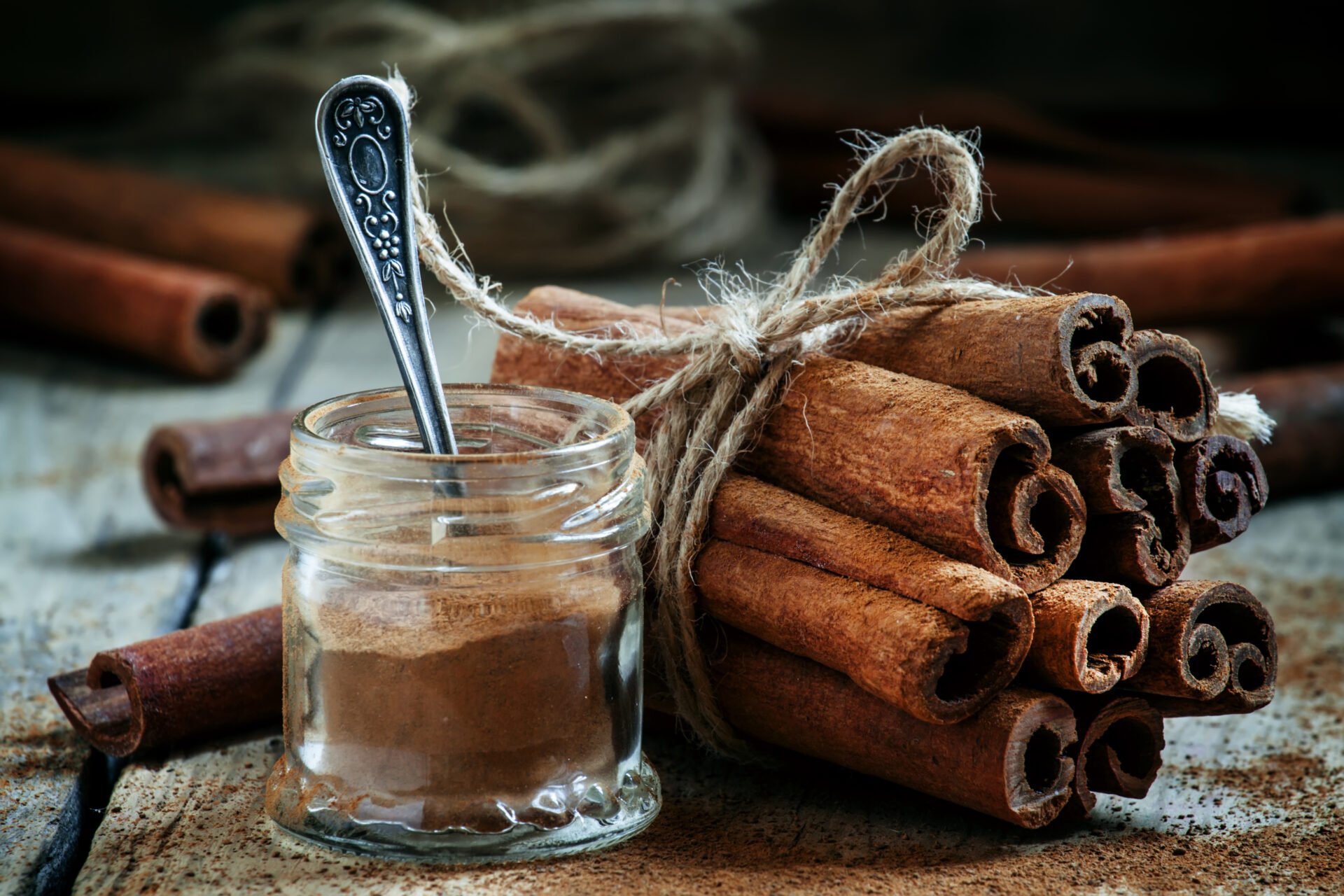 Ground cinnamon, cinnamon sticks, tied with jute rope on old wooden background in rustic style, selective focus