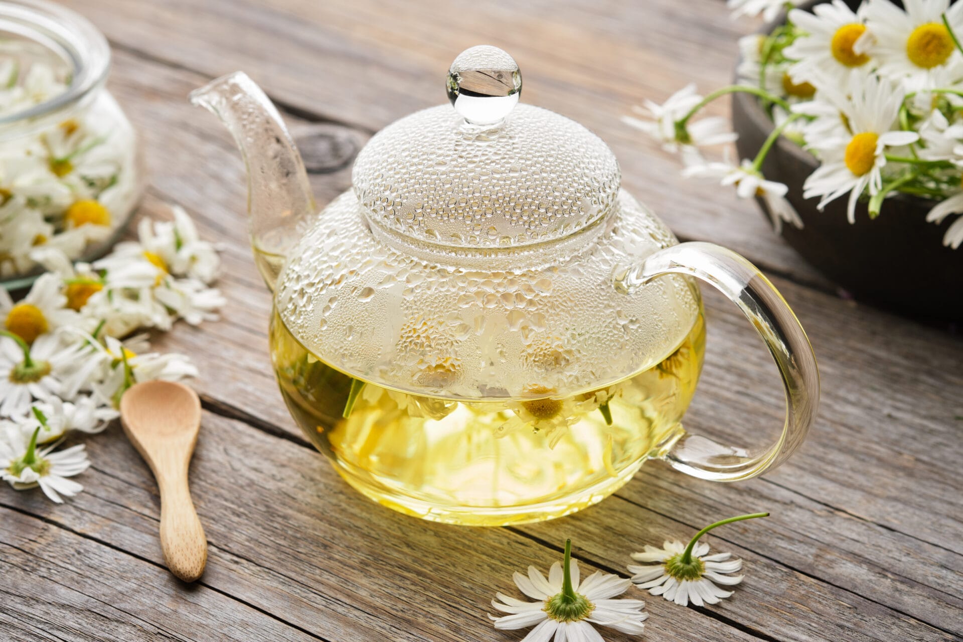 Chamomile daisy flowers on wooden table. Alternative herbal medicine. Glass tea kettle of healthy chamomile herbal tea. 